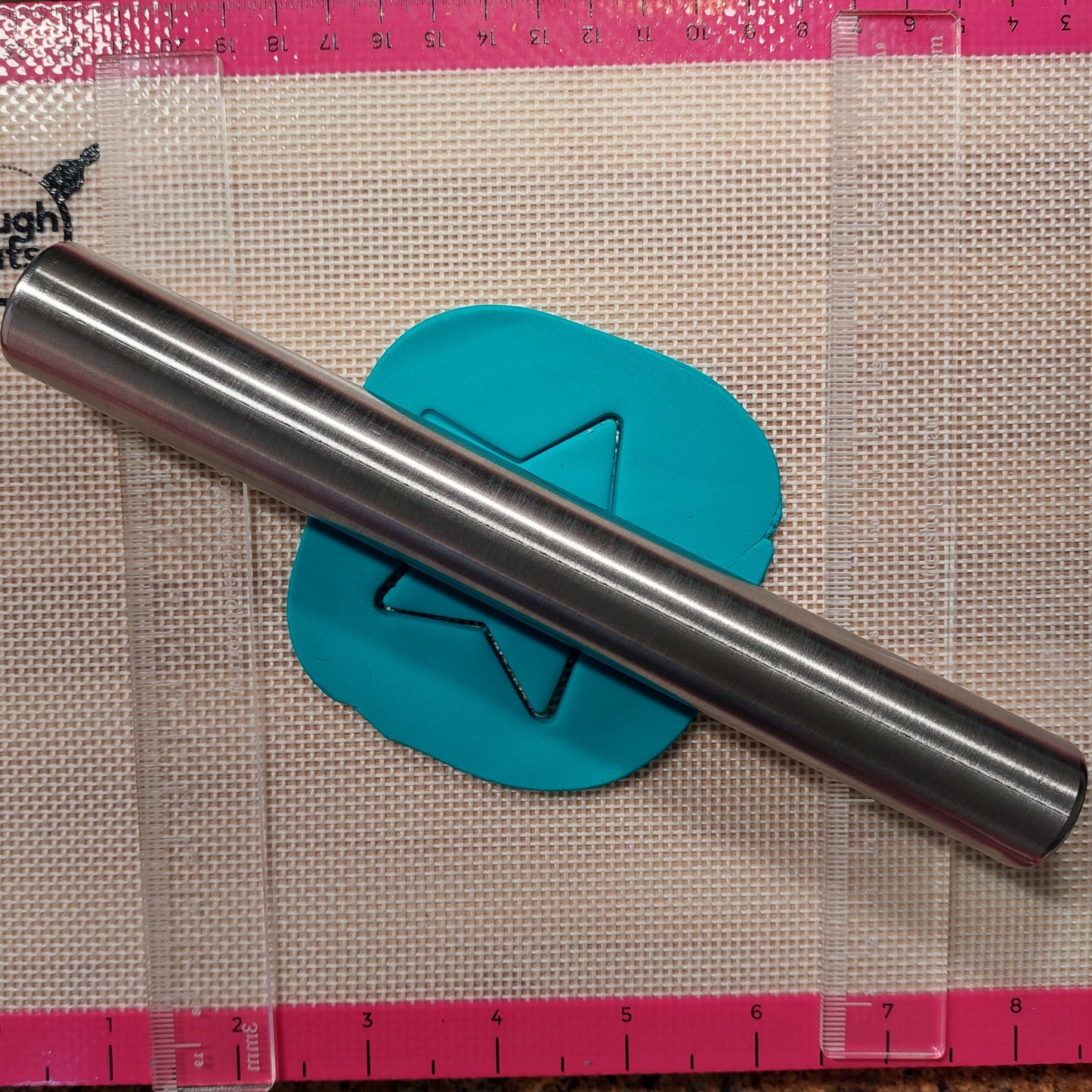 Metal rolling pin on a piece of teal fondant with a pink ruler on a textured surface