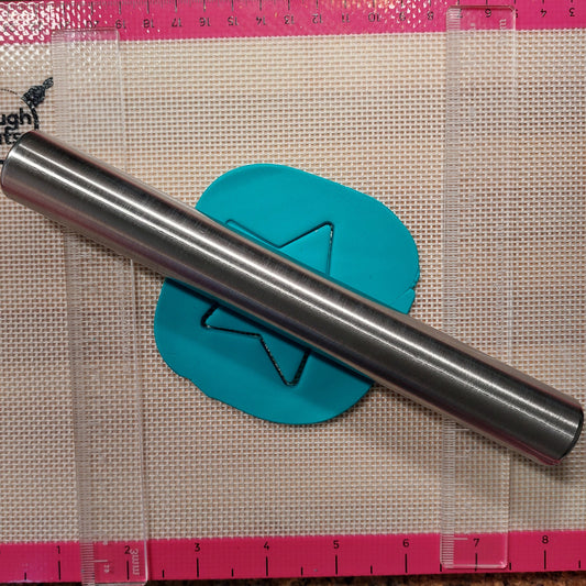 Metal rolling pin on a piece of teal fondant with a pink ruler on a textured surface
